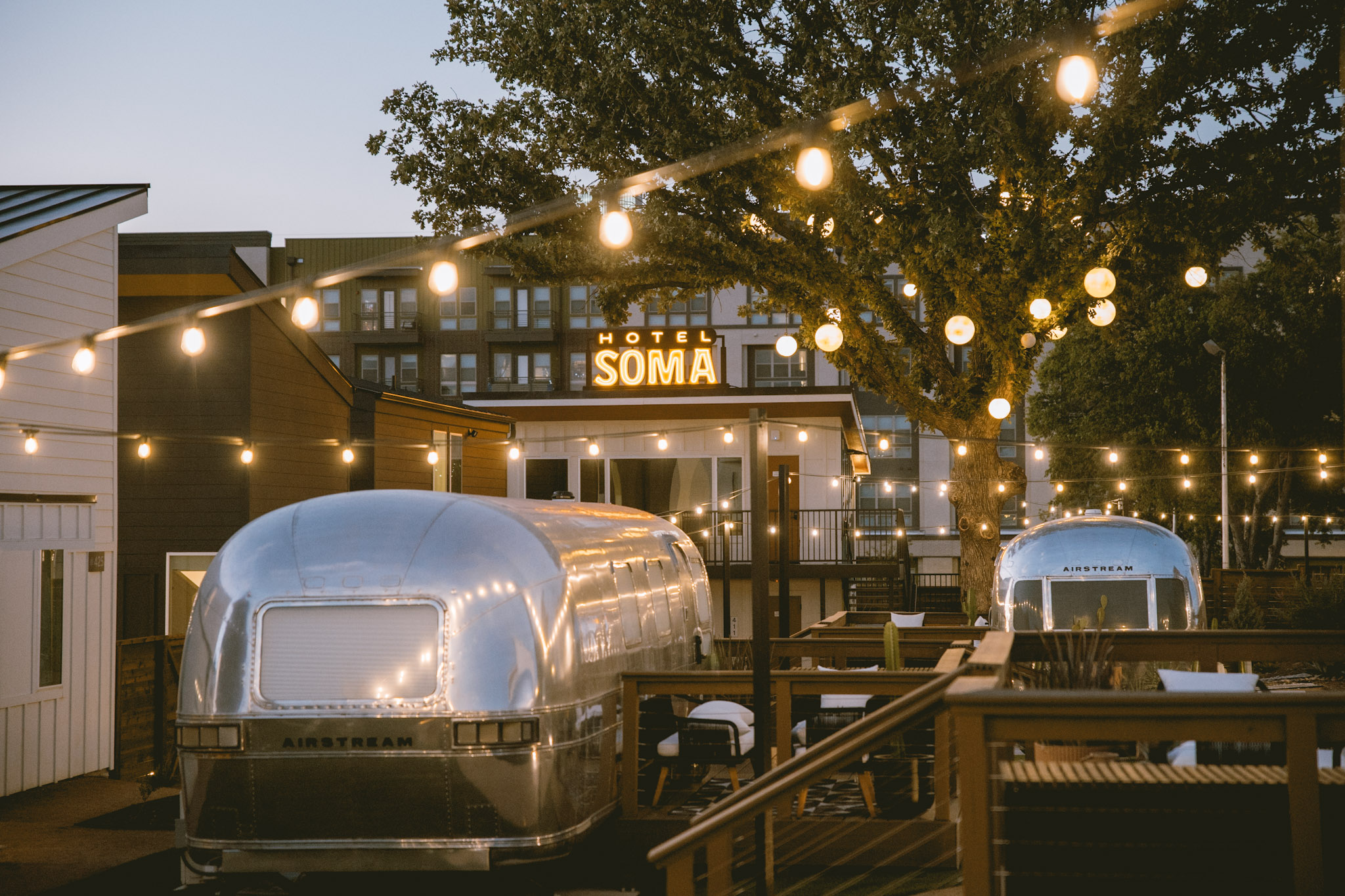 Airstream suites and their decks under string lights at dusk in the Hotel SOMA courtyard