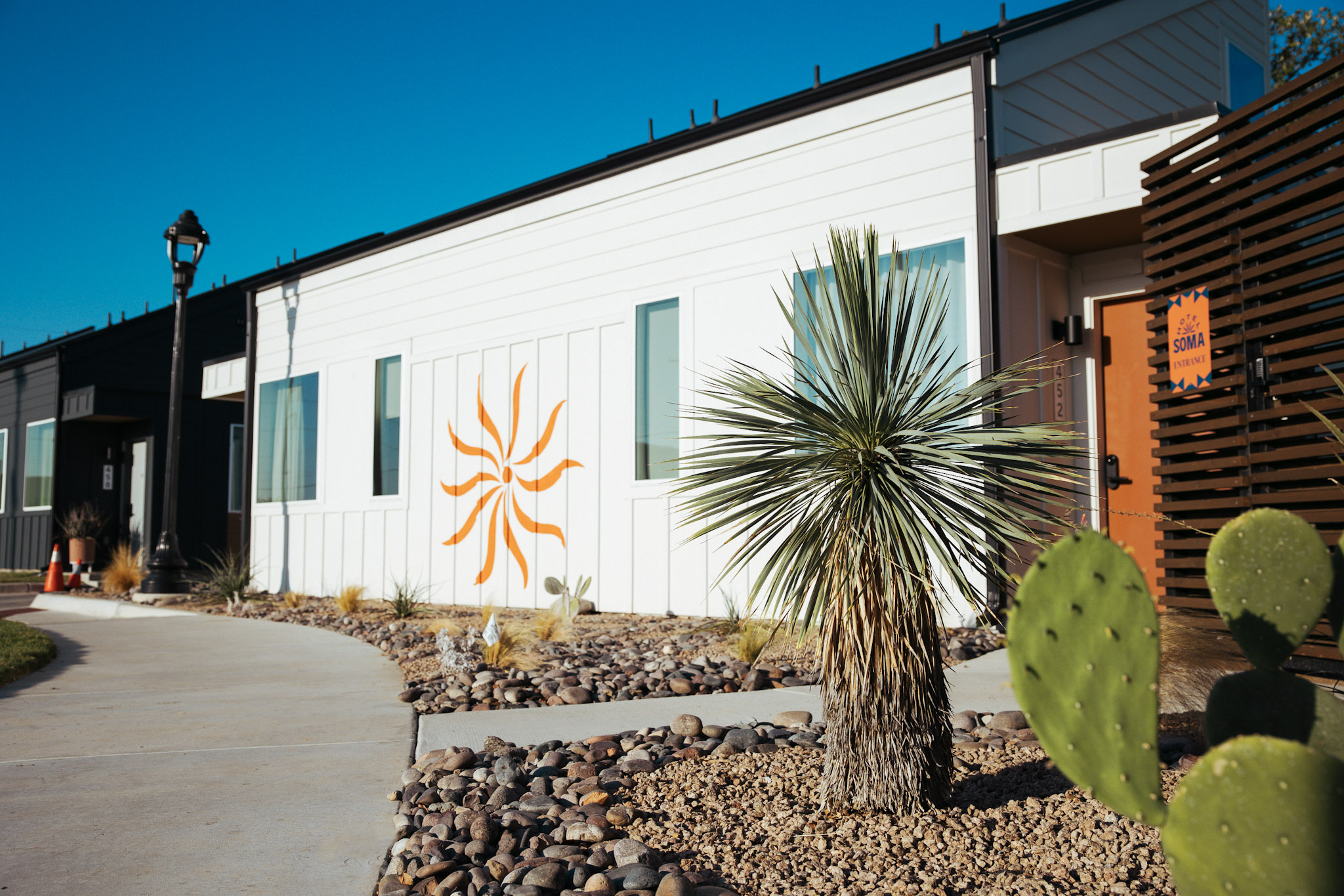 A white two-story casita with the orange SOMA pinwheel mural and desert landscaping at Hotel SOMA Fort Worth