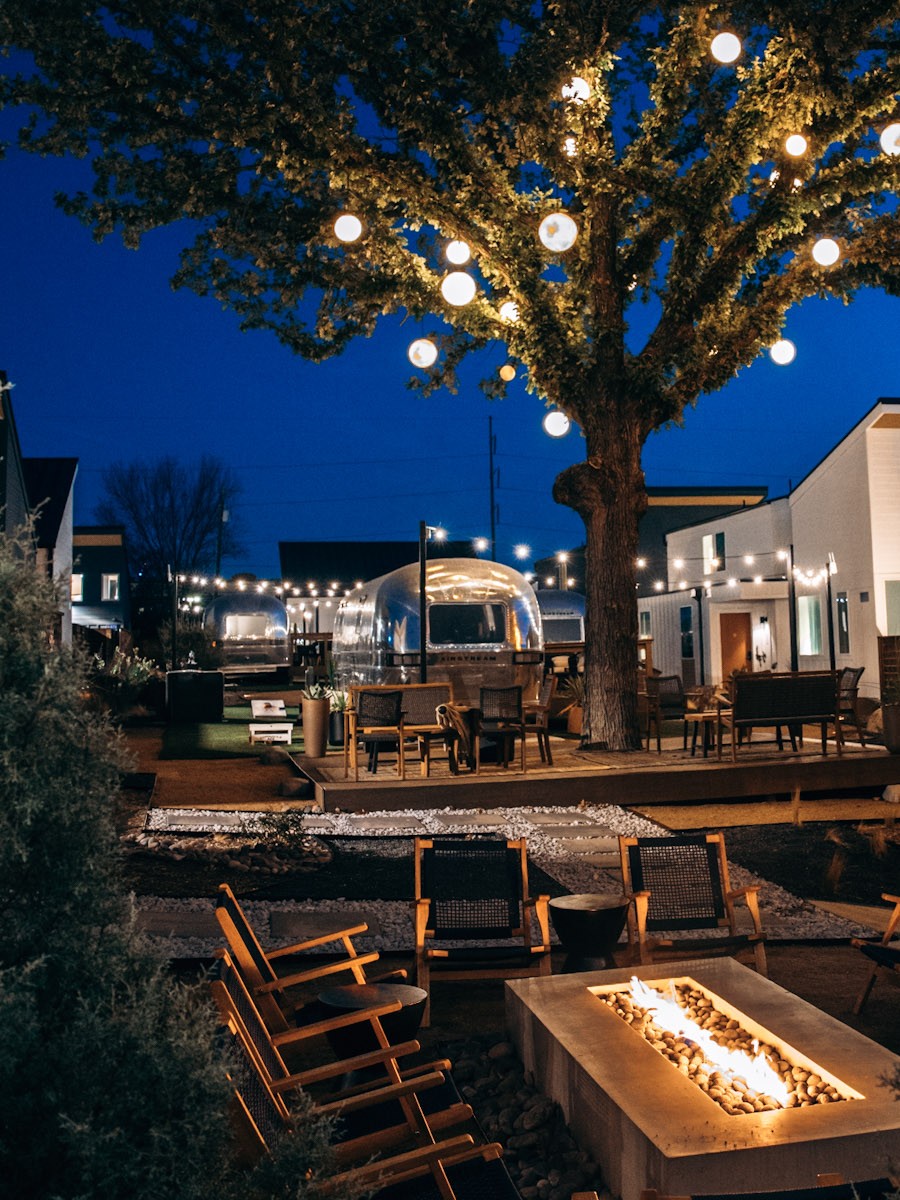 An Airstream suite beneath the lantern-lit oak, with the courtyard fire pit glowing at night at Hotel SOMA Fort Worth