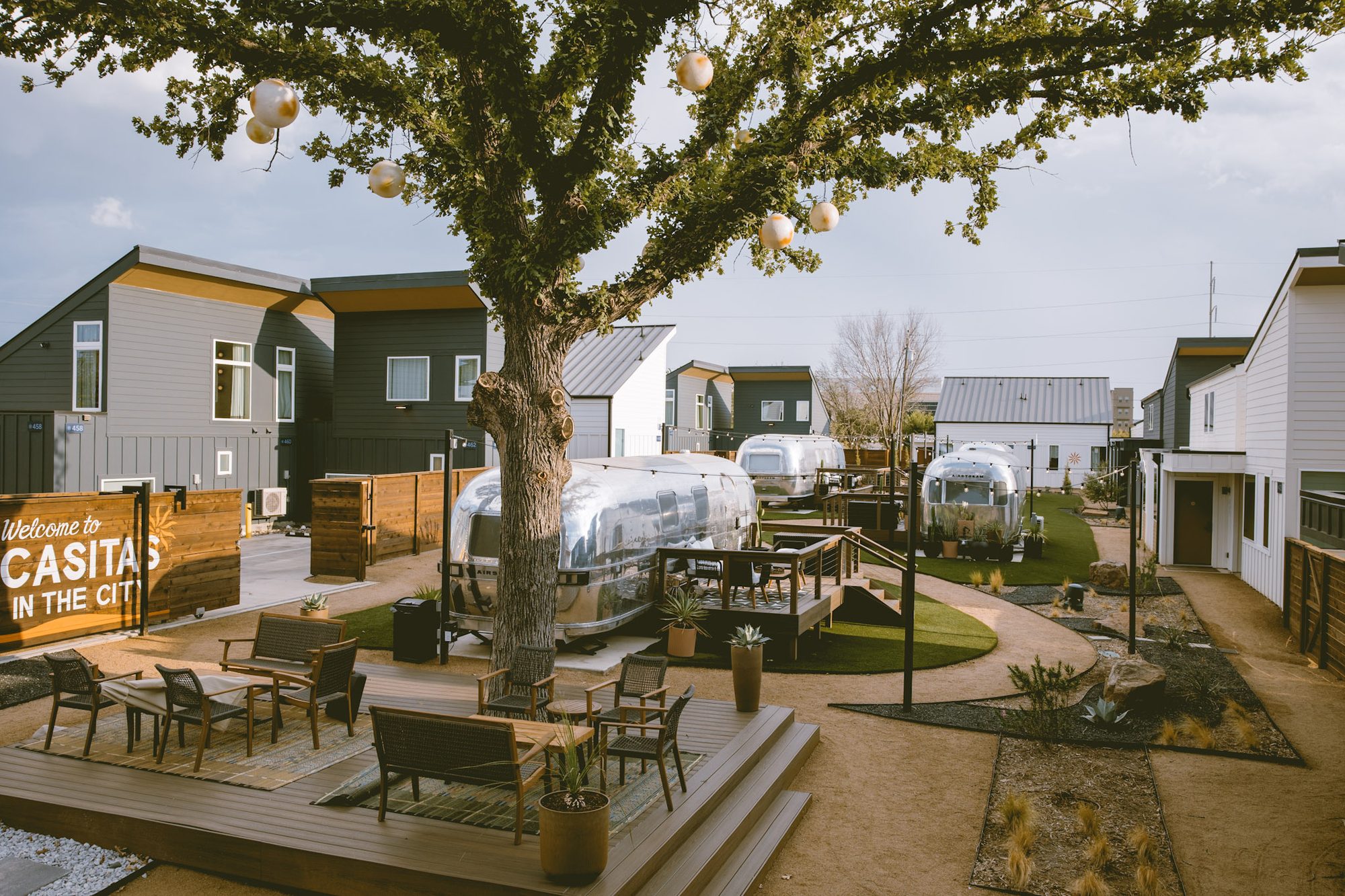 Daylight over the gated Hotel SOMA courtyard — the Welcome to Casitas in the City sign, live oak and Airstream suites in Fort Worth