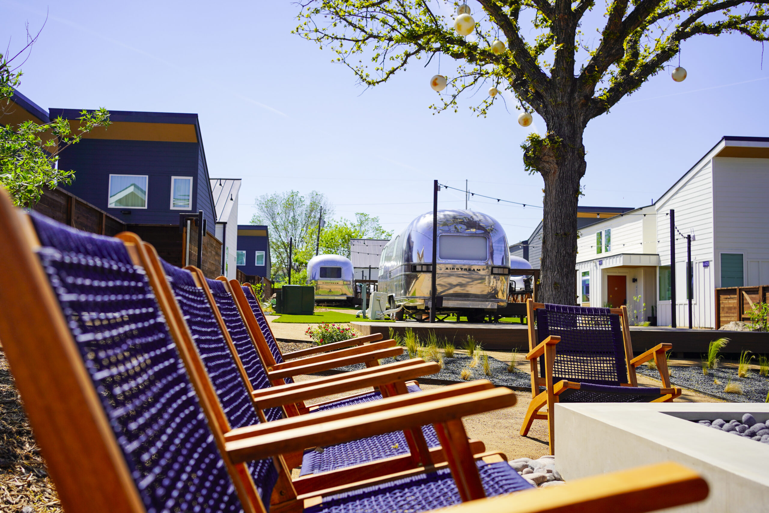 Lounge chairs around the fire-pit courtyard with an Airstream and oak tree